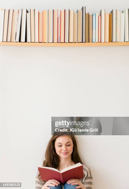 hispanic girl reading under bookshelf - teenagers reading stock pictures, royalty-free photos & images