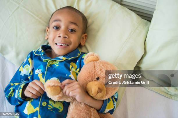 african american boy hugging teddy bear in bed - bear lying down stock pictures, royalty-free photos & images