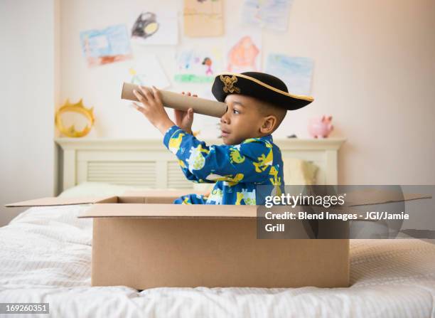 african american boy playing in cardboard box - boy sitting on bed stock-fotos und bilder