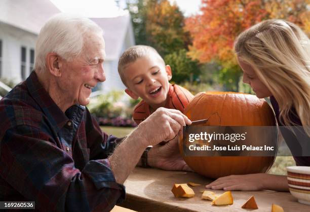 caucasian man carving pumpkin with grand children - fries stockfoto's en -beelden