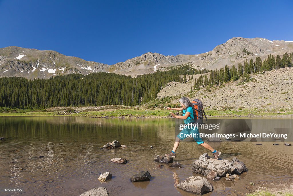 Hispanic hiker climbing on rocks in lake