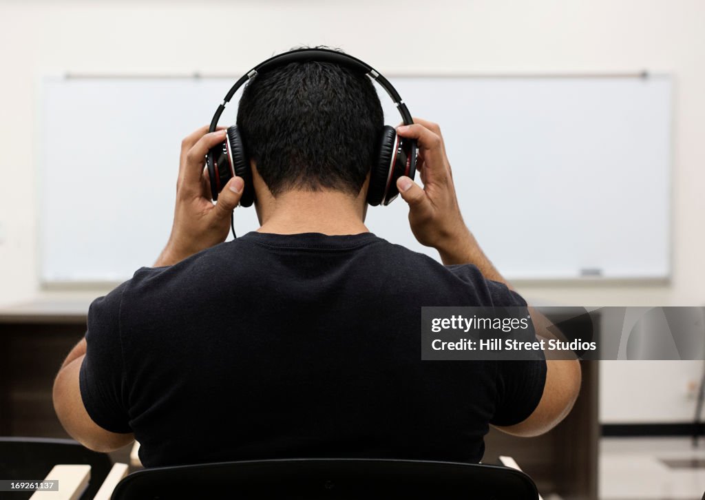 Hispanic student listening to headphones in classroom