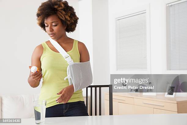 african american woman in sling taking medication - cabestrillo de brazo fotografías e imágenes de stock