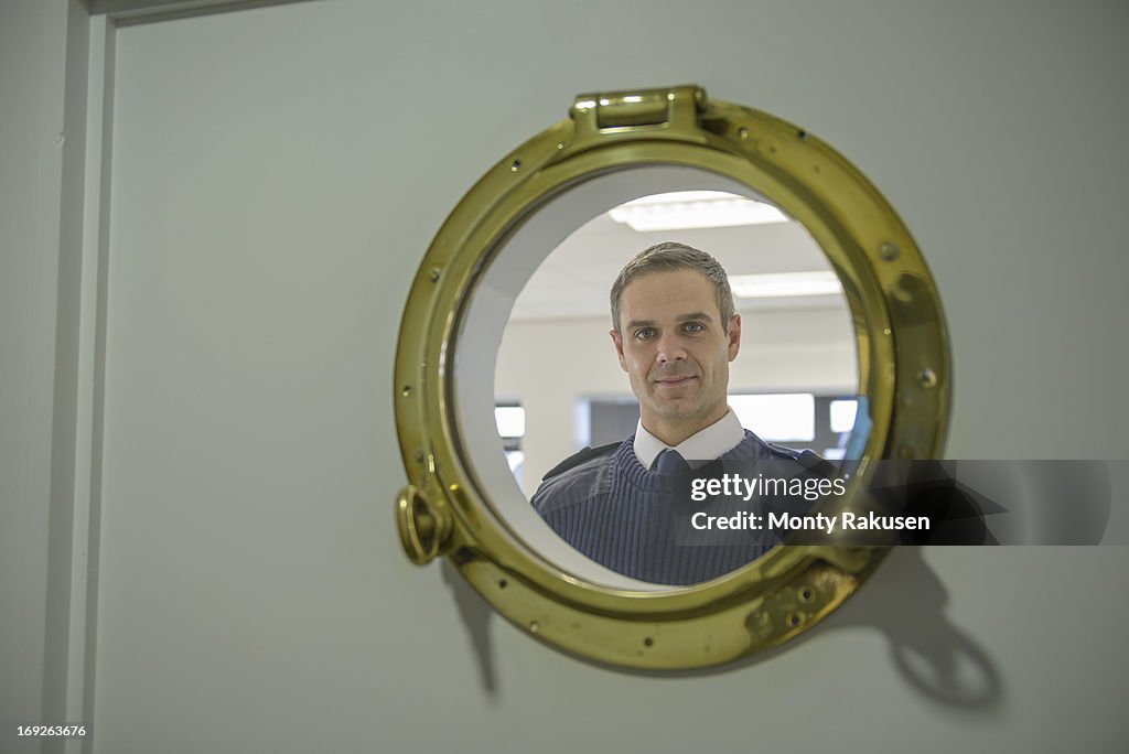 Portrait of shipping cadet looking through ship's porthole