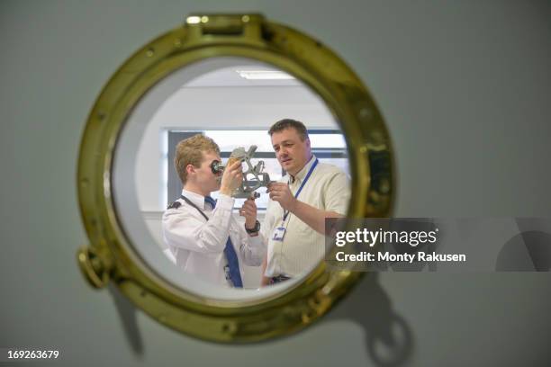 tutor teaching shipping cadet how to use sextant, view through ship's porthole - kadett stock-fotos und bilder