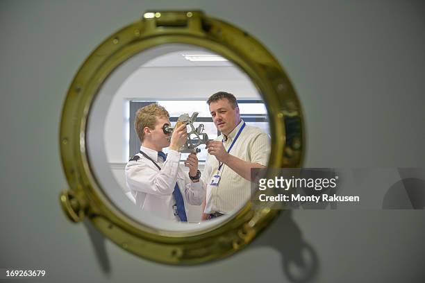 tutor teaching shipping cadet how to use sextant, view through ship's porthole - élève officier photos et images de collection