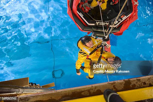 offshore oil workers hoisted from raft in sea ditching survival training in pool facility - 救命ボート ストックフォトと画像
