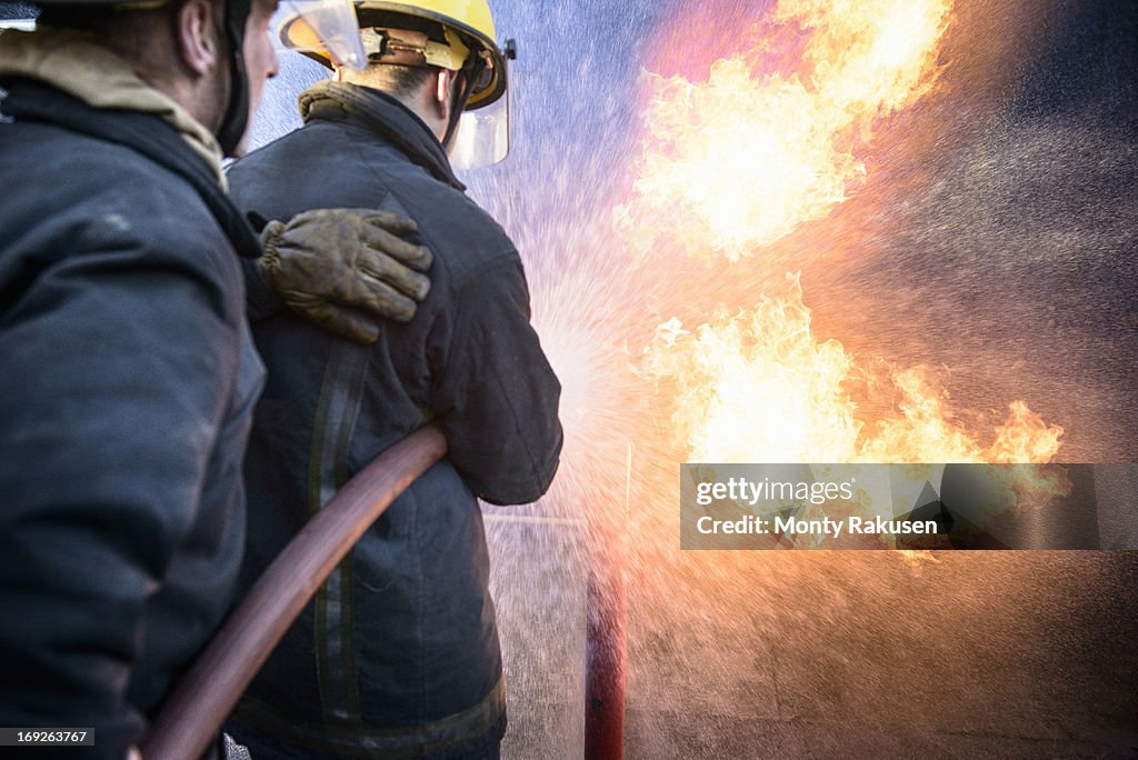 Two firefighters putting out fire in fire simulation training facility, rear view