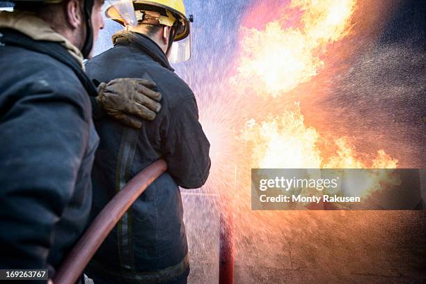 two firefighters putting out fire in fire simulation training facility, rear view - fireman uk stock pictures, royalty-free photos & images