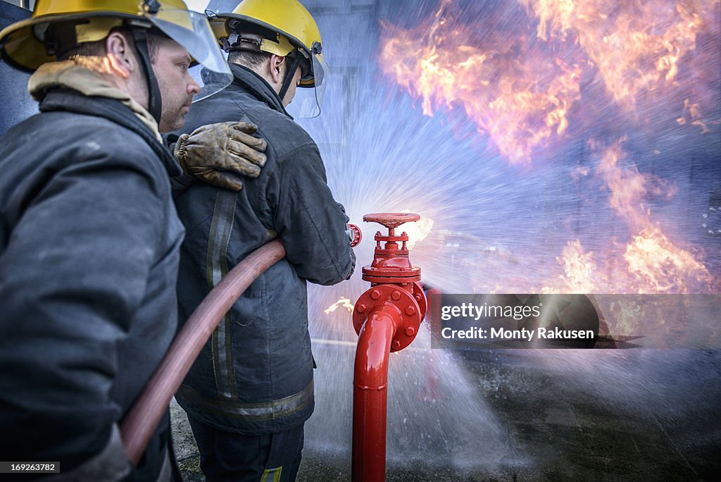 Two firefighters putting out fire in fire simulation training facility, rear view