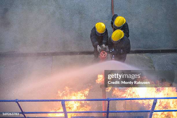 three firefighters putting out fire in fire simulation training facility, overhead view - firefighter stock pictures, royalty-free photos & images