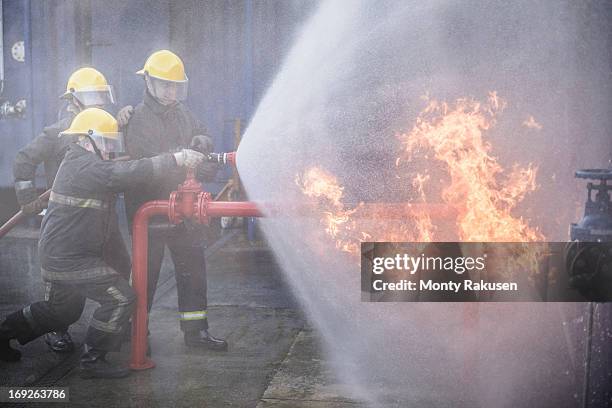 three firefighters putting out fire in fire simulation training facility - firefighter uk stock pictures, royalty-free photos & images