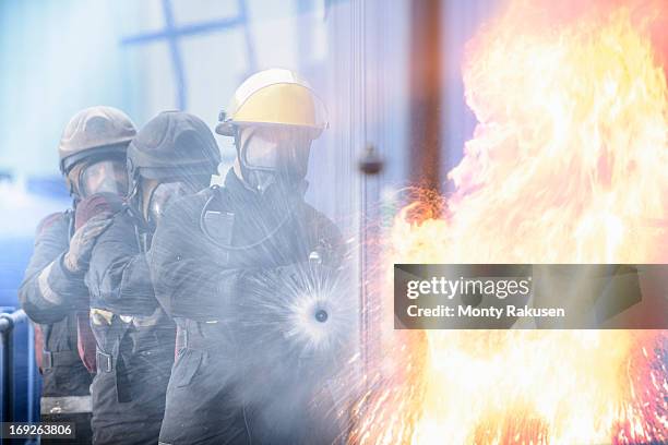 three firefighters using hose in fire simulation training facility, front view - fireman uk stock pictures, royalty-free photos & images