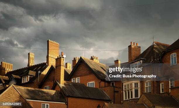 pitched roofs and chimneys of traditional brick houses in england - storm clouds stock pictures, royalty-free photos & images