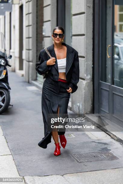 Gili Biegun wears white cropped top, black striped jacket, skirt with slit, red ankle boots, Valentino bag outside Iceberg during the Milan Fashion...