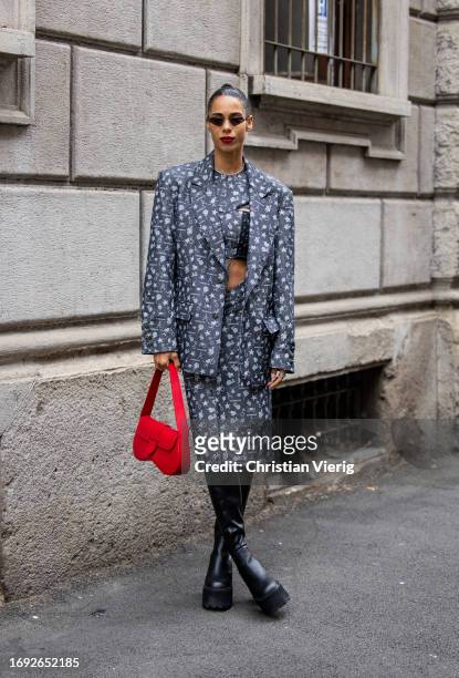 Guest wears grey jacket, skirt with graphic print, black boots, red bag outside Iceberg during the Milan Fashion Week - Womenswear Spring/Summer 2024...