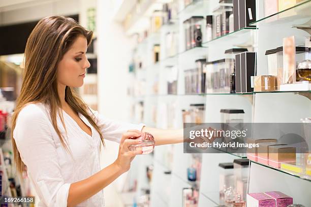 woman trying on fragrances in store - magasin cosmétique photos et images de collection