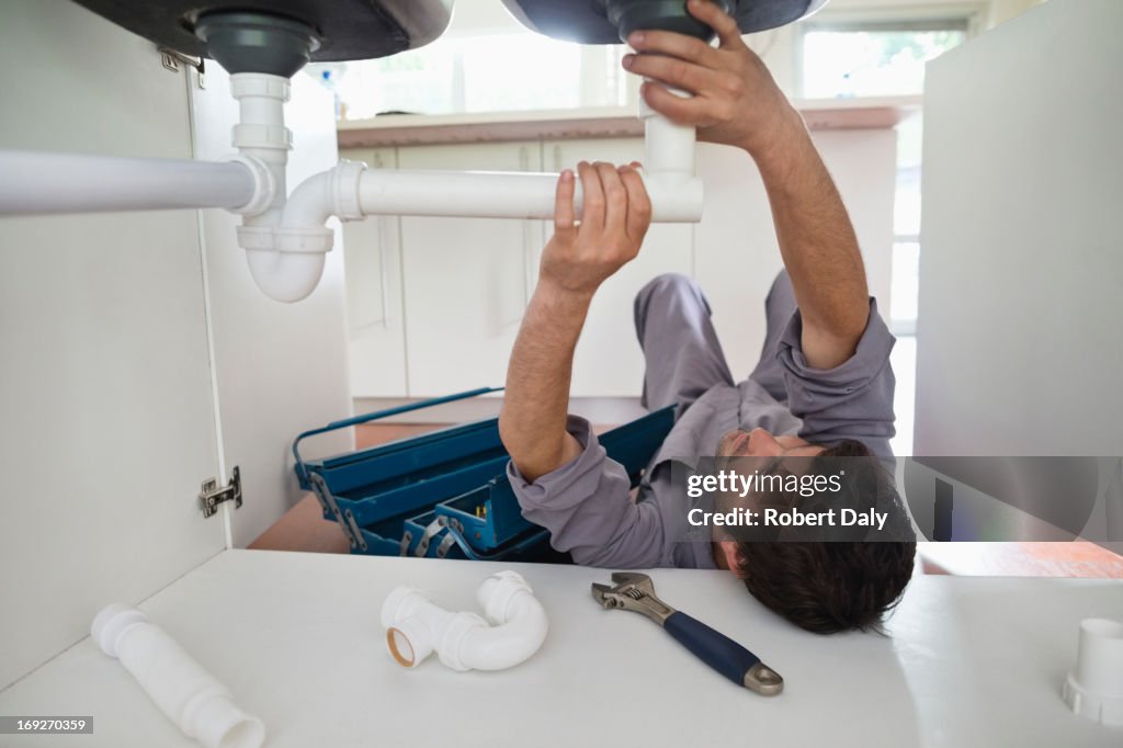 Plumber working on pipes under kitchen sink