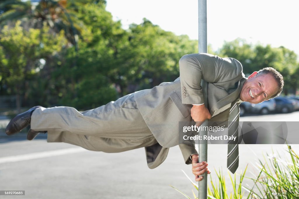 Businessman balancing on pole on city street