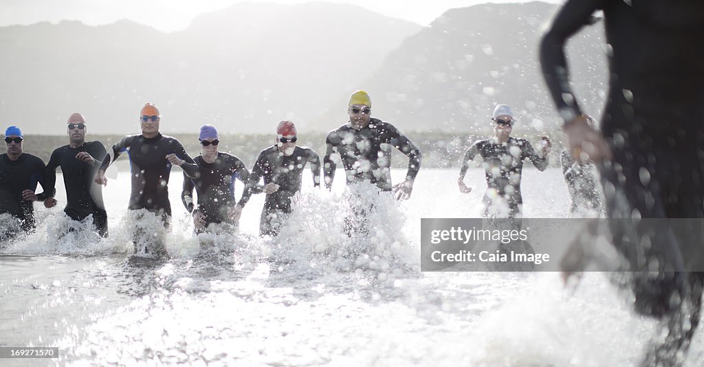 Triathletes in wetsuits running in waves