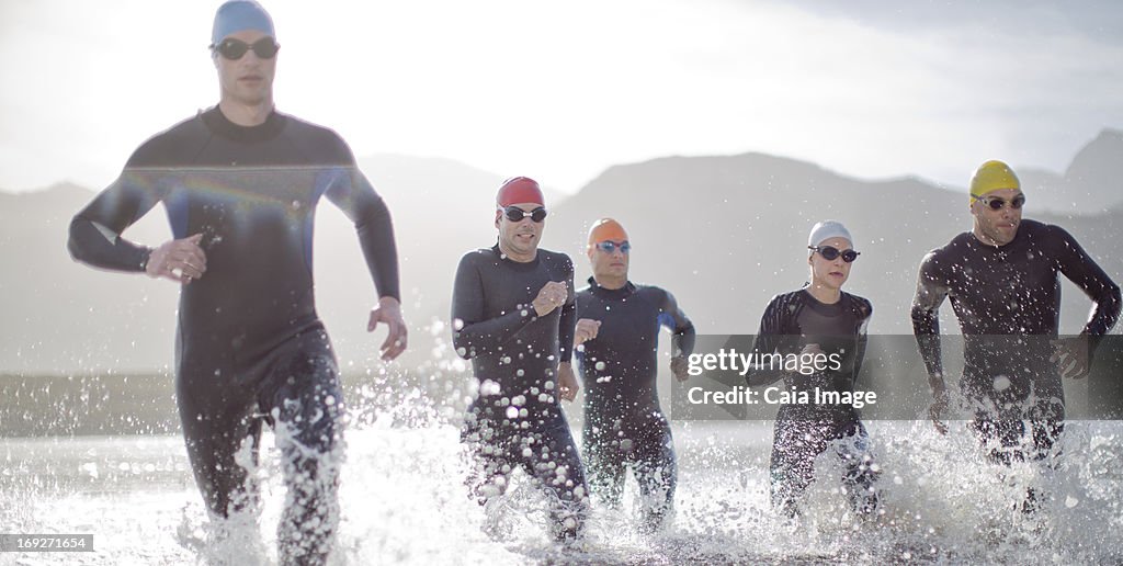 Triathletes in wetsuits running in waves