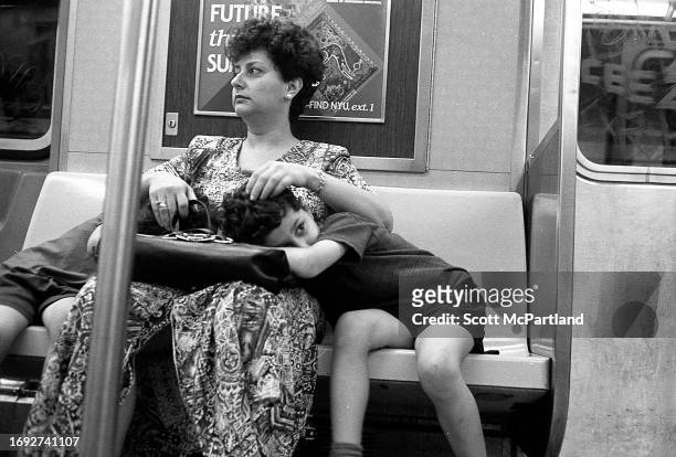 View of a woman with two children lying on her lap, as they ride the subway, Queens, New York, New York, May 23, 1998.