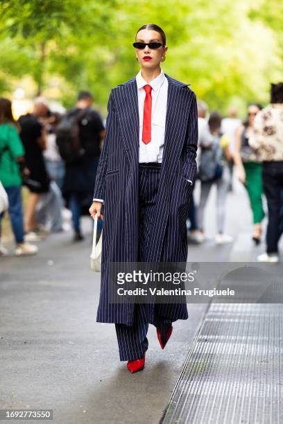Guest is seen wearing black sunglasses, gold round earrings, a red tie, a white shirt, red leather shoes, a white leather bag and a striped blue and...