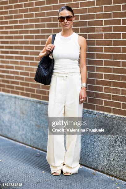 Guest is seen wearing black and orange sunglasses, a white tank top, white cream wide leg high waist trousers, white cream leather sandals and a...
