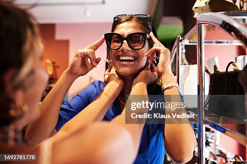 Happy woman trying sunglasses by friends in mall