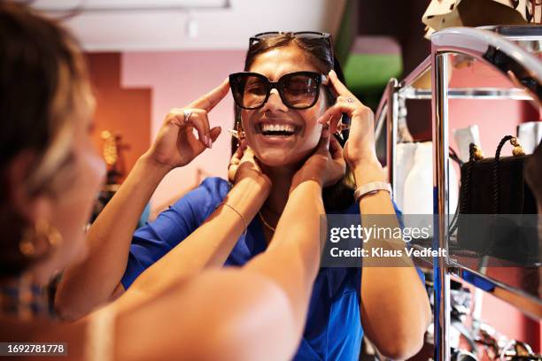 happy woman trying sunglasses by friends in mall - retro style shopping stock pictures, royalty-free photos & images