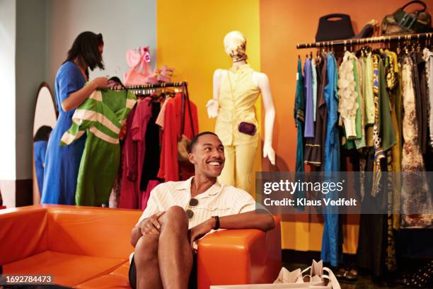 happy young man sitting on sofa in store - blue dress hanger stock pictures, royalty-free photos & images