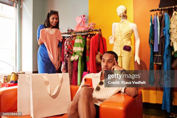 contemplative man with smart phone on sofa in store - dial stock pictures, royalty-free photos & images