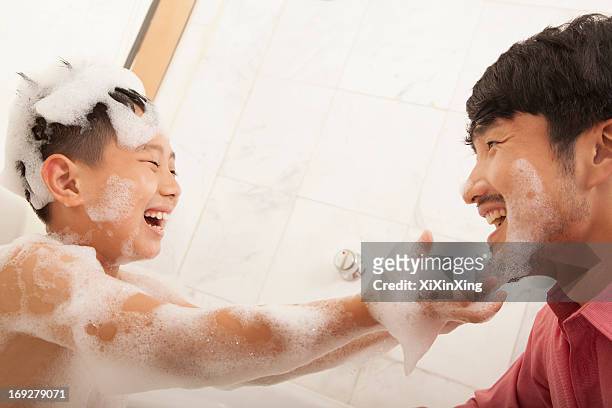 son in bathtub puts soap on his father's face - red tub 個照片及圖片檔