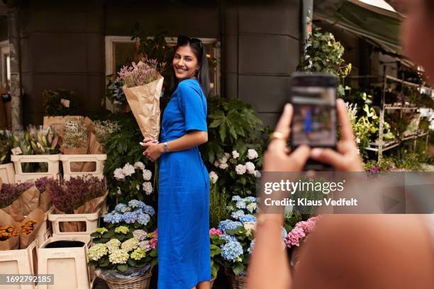 woman photographing friend with flower bouquet - blue dress stock pictures, royalty-free photos & images