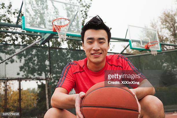 young man sitting with a basketball on the basketball court, portrait   - young man holding basketball stockfoto's en -beelden