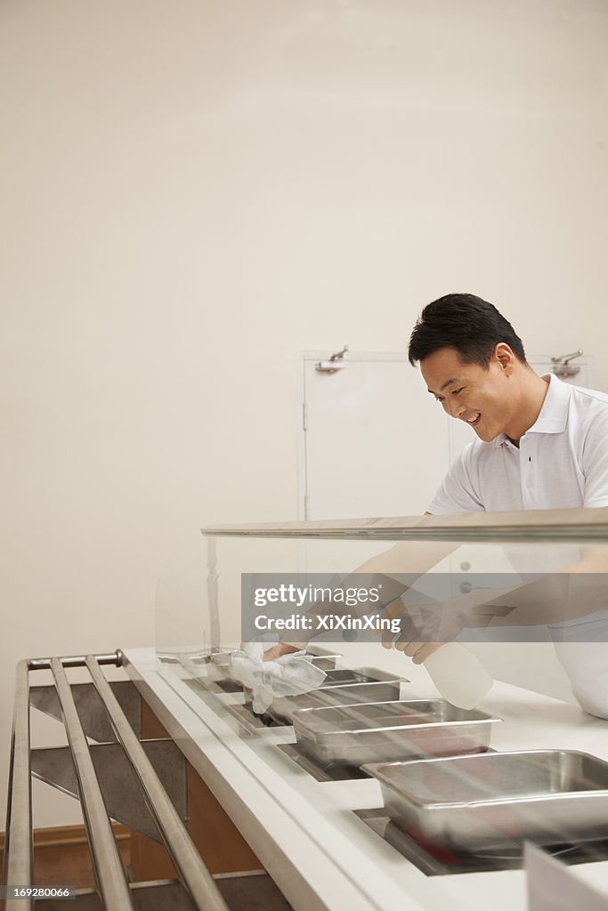 Cafeteria worker cleaning food serving area