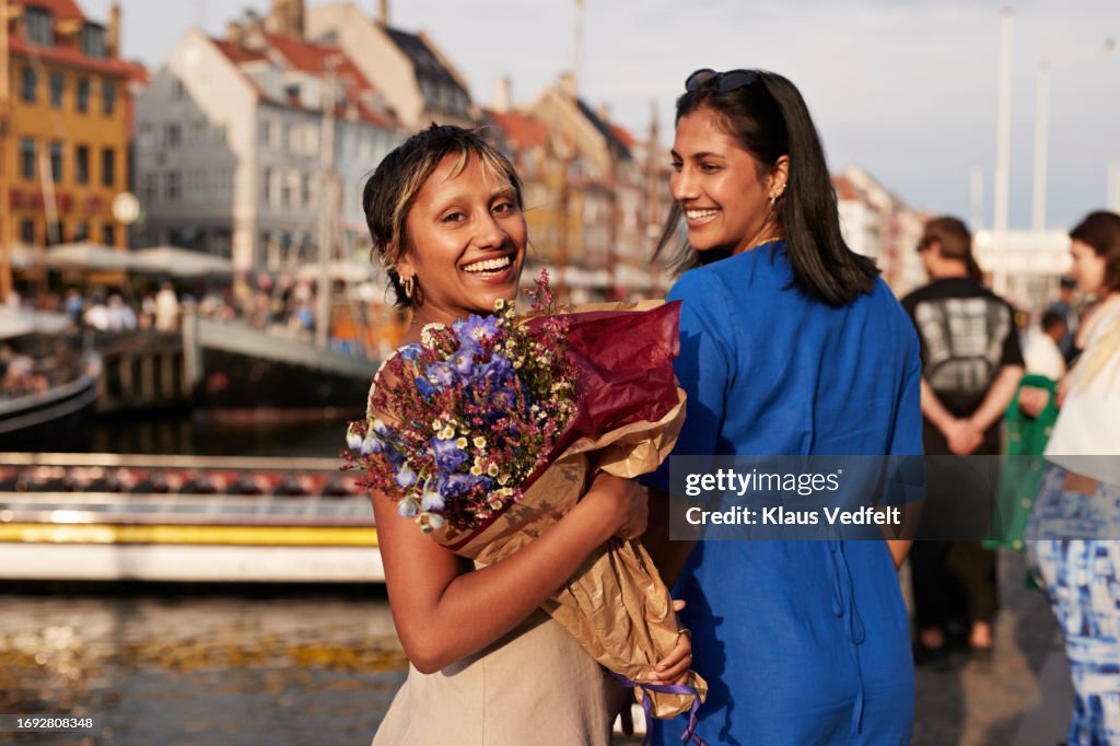 Smiling young with flower bouquet by female friend