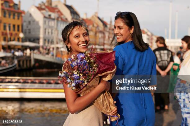 smiling young with flower bouquet by female friend - copenhagen nyhavn stock pictures, royalty-free photos & images