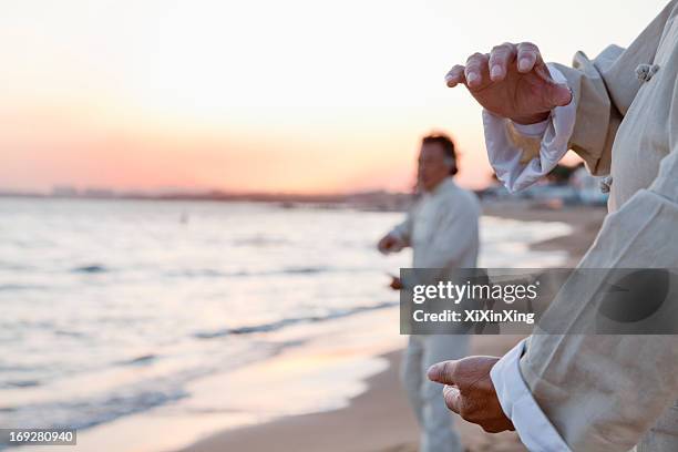 two older people practicing taijiquan on the beach at sunset, close up on hands - tai chi imagens e fotografias de stock