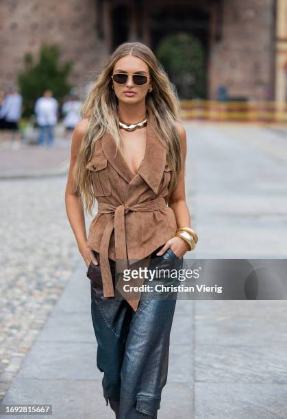 Romee Strijd wears brown belted wild leather vest, blue metallic mixed colors pants, necklace outside Alberta Ferretti during the Milan Fashion Week...