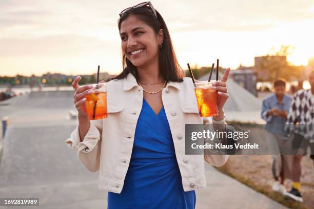 smiling young woman walking with juice glasses - cold drink stock pictures, royalty-free photos & images