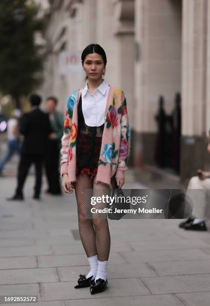 Guest is seen outside Molly Goddard show wearing white shirt, colorful wool cardigan, red lace pants, black net tights, white socks, black leather...