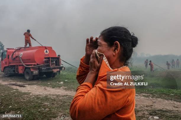 Woman reacts amidst smoke as firefighters try to protect houses from a wildfire in Ogan Ilir, South Sumatra, on September 27, 2023.