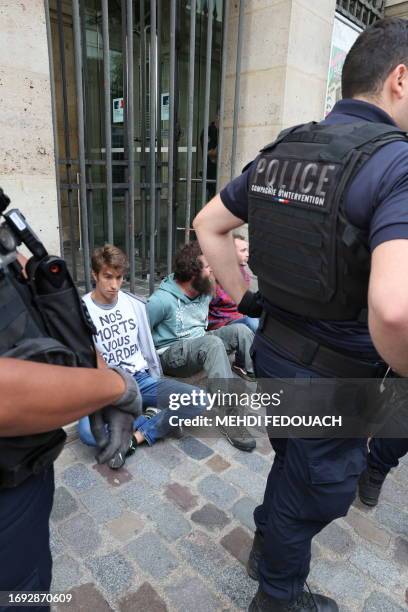 Activists of environmental group "Derniere renovation" arrested by French police officers sit on the ground in front of the French Ministry of the...