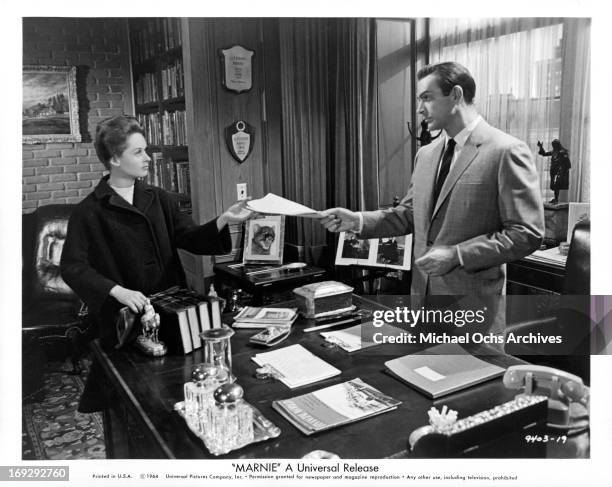 Tippi Hedren is handed a work assignment by Sean Connery in a scene from the film 'Marnie', 1964.