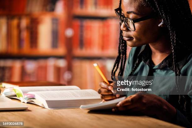 young woman reading a book and studying for exam at the library - examination table bildbanksfoton och bilder