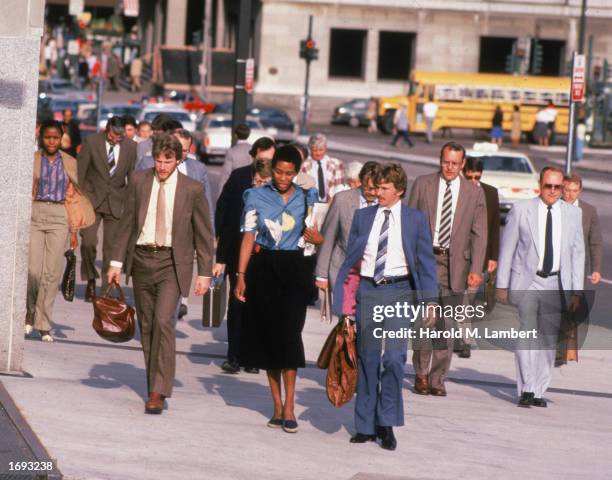 Business people carry briefcases while walking on a city street, 1980s.