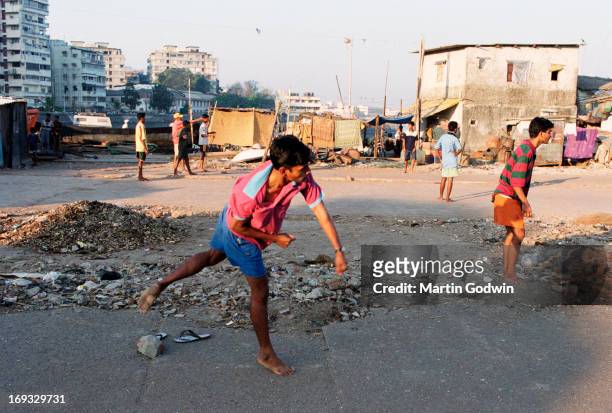 Boys playing cricket in the slum area of Mumbai with boy bowling ball in foreground, February 2003
