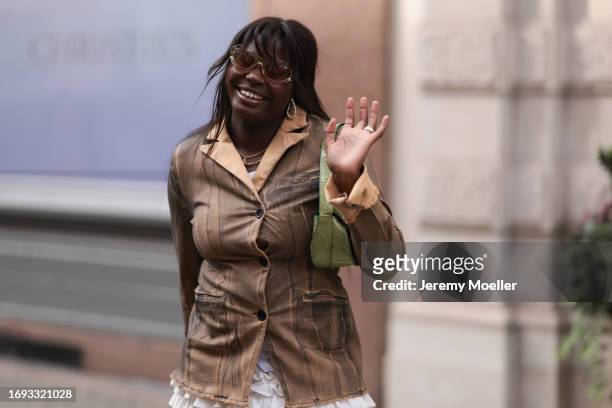 Guest is seen outside Molly Goddard show wearing yellow sunnies, black and orange colored buttoned up blazer, green leather shoulder bag and white....