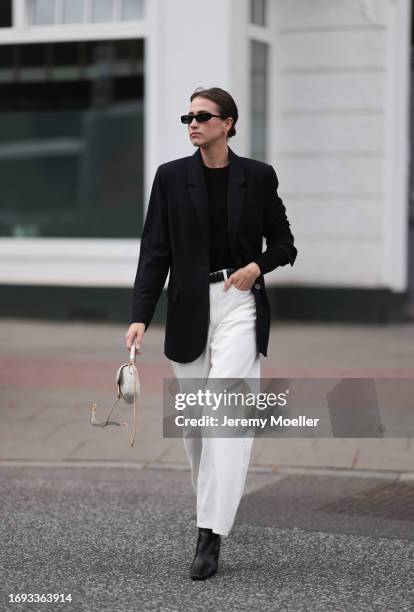 Marie Danker is seen wearing black narrow sunglasses from Carolina Lemke, golden hoop earrings from Missoma, a black long blazer with shoulder pads...